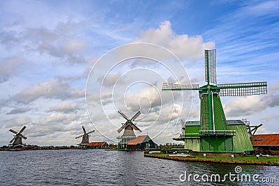 Green windmills and grasslands along the canal on a clear day. Beautiful clouds in Zaanse Schans Stock Photo