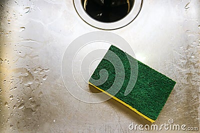 Green and yellow scrubing sponge lying in scratch and wet sink with garage disposal Stock Photo