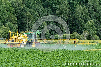 Green and yellow tractor fertilizing a green potato field Editorial Stock Photo