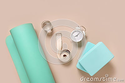 Green yoga mat, two wooden blocks, water, clock and white belt. Yoga practice, relaxation and meditation concept. Stock Photo