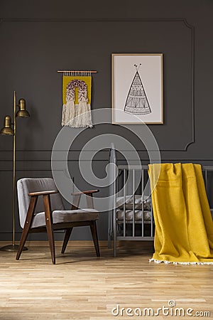 Grey armchair next to bed with yellow blanket in baby`s bedroom Stock Photo