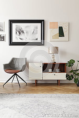 Grey armchair next to white cabinet with lamp in modern loft interior with posters. Real photo Stock Photo