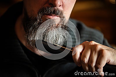 Grey bearded man with a straightener, beard styling and care at home Stock Photo