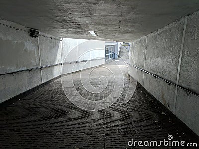 A grey, brutalist, concrete underpass leading down to a brightly lit entrance Stock Photo