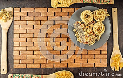 A grey ceramic plate with dry fettuccine paste on a bamboo stacked substrate and bamboo spatulas with various pastes on a dark Stock Photo