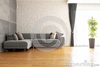 Grey corner couch on wooden floor against brick wall in bright a Stock Photo