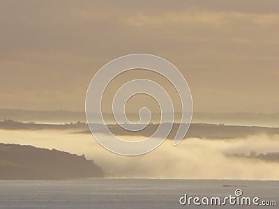 A grey seascape as fog rolls down the River Fowey to meet the sea at sunrise on a cloudy early morning in Cornwall England Stock Photo