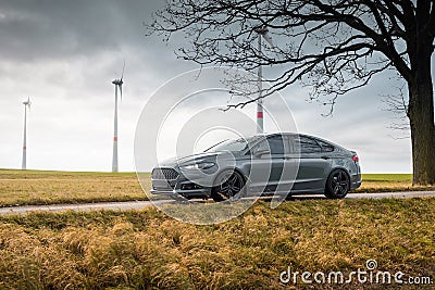 grey Ford Mondeo on a narrow road in a field with wind turbines Editorial Stock Photo