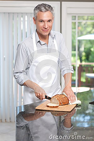 Grey hair man cutting bread in apron Stock Photo