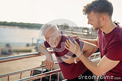 Grey-haired male holding hand on his chest young male helping him Stock Photo