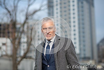 Grey-haired man wearing a grey coat looking serious Stock Photo