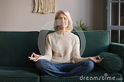 Grey haired mature woman meditating, practicing yoga at home Stock Photo