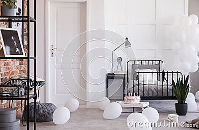 Grey lamp and clock on nightstand next to single metal bed in industrial bedroom with balloons Stock Photo