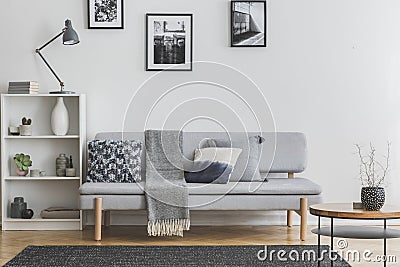 Grey lamp on white bookshelf with vases and books next to elegant settee Stock Photo