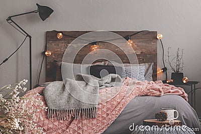 Grey and pastel pink blanket on grey bedding of fashionable bedroom with rustic design Stock Photo