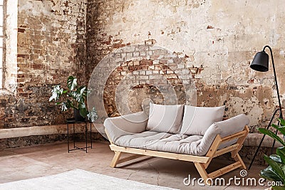 Grey sofa between plant and black lamp in wabi sabi loft interior with red brick wall Stock Photo