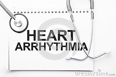 Grey stethoscope and paper plate with a sheet of white paper with text Heart arrhythmia light blue backround. Medical concept Stock Photo