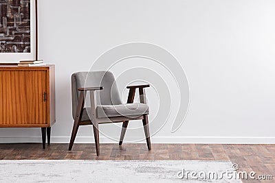 Grey vintage armchair next to retro cabinet with books, warm carpet on wooden fool, real photo Stock Photo