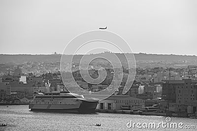 Greyscale of a port with numerous building on the background and a big ferry in the front in Valleta Editorial Stock Photo