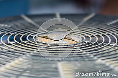 Grill of the fan of heavy duty central air conditioner system and running fan in the background Stock Photo