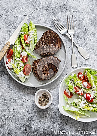 Grilled beef steak and fresh romaine salad cherry tomatoes yogurt dressing salad on a grey background, top view Stock Photo