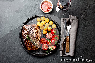 Grilled beef steak served on cast iron plate with tomato salad, potatoes balls and red wine. Barbecue, bbq meat beef Stock Photo