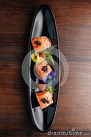 Grilled Medium Rare Salmon Cube topping with caviar and served with strawberry and orange in black plate Stock Photo