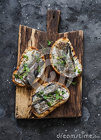 Grilled bread sardines micro greens sandwiches on a rustic cutting board on a dark background, top view Stock Photo