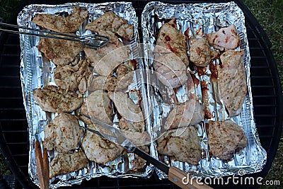 Grilled chicken breast slices placed on alluminium plates on grill, turned by steel forceps and fork during barbecue process. Stock Photo