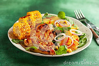 Grilled chicken breasts cooked on a BBQ served with citrus salad and corn on a plate. Close up view. Concept homemade summer Stock Photo