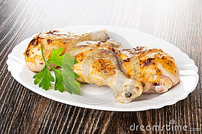 Grilled chicken legs, leaves of parsley in dish on wooden table Stock Photo