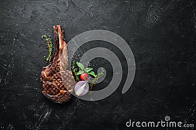 Grilled cowboy beef steak, herbs and spices on a black stone background. Barbecue. Top view. Stock Photo