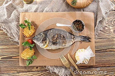 Grilled dorado fish with lemon and potato wedges on wooden board and glass of beer on wooden table Stock Photo