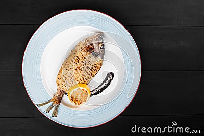 Grilled dorado fish with lemon and truffle sauce on plate on wooden background. Stock Photo