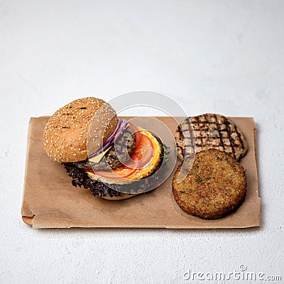 Grilled double or triple meat burger with tomatoes, onion and lettuce on parchment paper. Set of ingredients for super Stock Photo