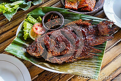 Grilled gurami or grilled gurame with red barbecue sauce, vegetables and chili sauce served on banana leaves Stock Photo