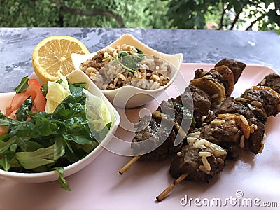 Grilled lamb on a skewer with rice, salad and fresh herbs. Stock Photo