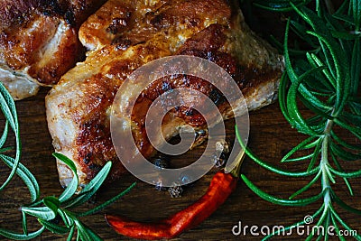 Grilled meat pieces dark crust on the outside and fresh rosemary on a wooden cutting board background. Stock Photo