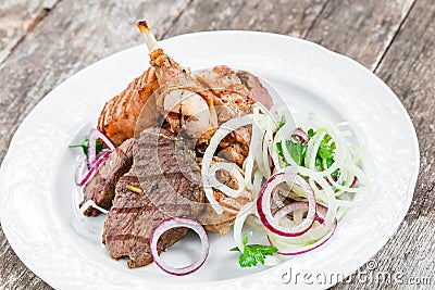 Grilled meat on plate, chicken legs, beef steak and onion on wooden background close up. Stock Photo