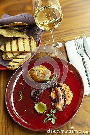 Grilled octopus on a red plate in a restaurant. Beautifully decorated dinner with white wine. Stock Photo