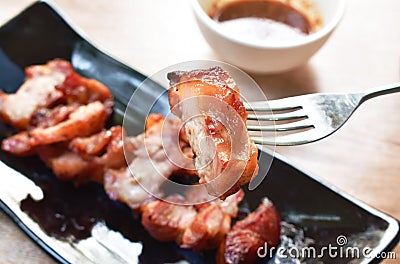 Grilled pork neck slice on plate stabbing on silver fork dipping spicy sauce Stock Photo