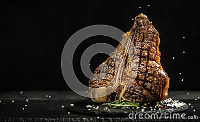 Grilled Premium Dry Aged T-bone Steak or porterhouse steak adding salt in a freeze motion on black background. USDA Prime Beef. Stock Photo