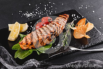 Grilled salmon fillet garnished with spinach, lemon, herbs on plate over wooden background. Hot fish dish Stock Photo