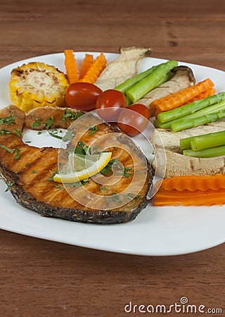 Grilled salmon steak slides until cooked, placed on a white plate with lemon on fish and vegetables, placed around the dish on a Stock Photo