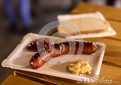 A grilled sausage on a paper plate with mustard and ketchup and a slice of bread, a typical meal sold at outdoor Christmas markets Stock Photo