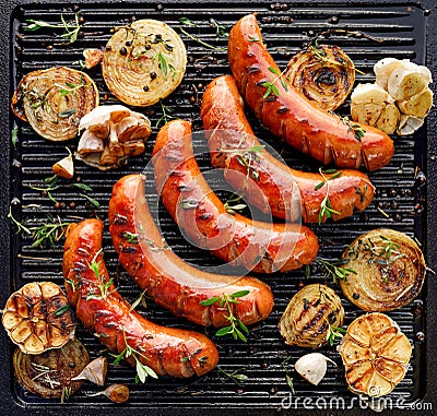 Grilled sausages with the addition of herbs and vegetables on the grill plate, top view. Stock Photo
