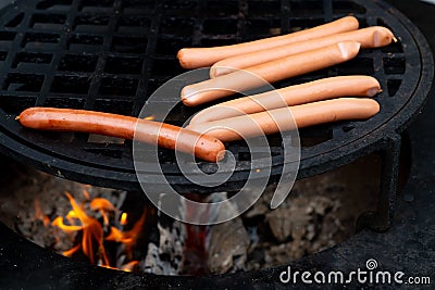 Grilled sausages on grill with smoke and flame on dark background Stock Photo