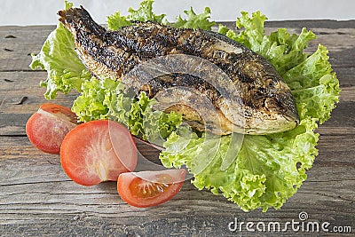 Grilled Sparus aurata with tomatoes and green salad on wooden background Stock Photo