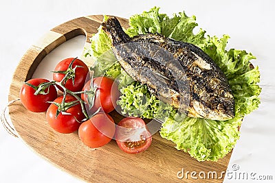 Grilled Sparus aurata with tomatoes and green salad on wooden background Stock Photo