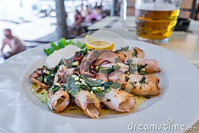 Grilled squids with herbs, garlic and lemon on white plate close-up. Popular and delicious Mediterranean meal Stock Photo